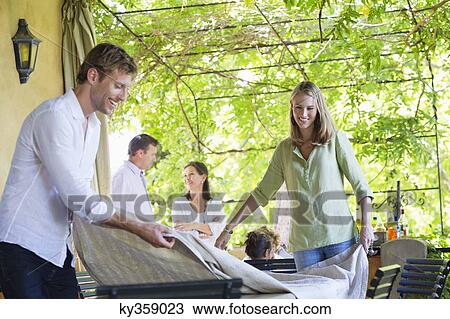 Couple placing tablecloth with family in the background View Large Photo Image Stock Image - Couple placing tablecloth with family in the background. Fotosearch