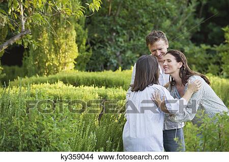 Picture - Mature couple hugging their mother in a garden. Fotosearch