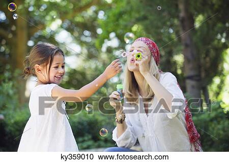 Stock Image - Mother and a little girl playing with bubble wand outdoors. Fotosearch