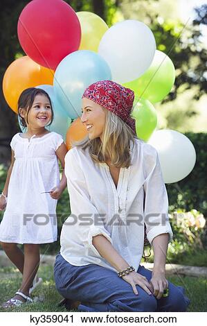 Stock Image - Mother looking at a little girl holding balloons. Fotosearch
