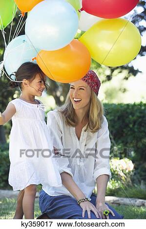 Stock Photo - Mother looking at a little girl holding balloons. Fotosearch
