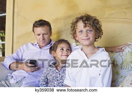 Portrait of a little boy with sister and father using a mobile phone while sitting on couch View Large Photo Image Stock Photo - Portrait of a little boy with sister and father using a mobile phone while sitting on couch. Fotosearch