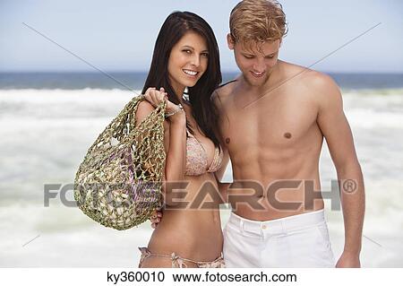Cheerful young couple standing on a beach View Large Photo Image Stock Image - Cheerful young couple standing on a beach. Fotosearch