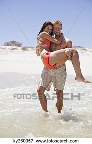 Man carrying woman on the beach View Large Photo Image Stock Photo - Man carrying woman on the beach. Fotosearch