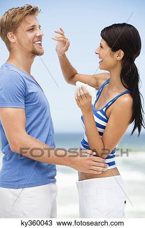 Stock Image - Woman applying suntan lotion on man's face. Fotosearch