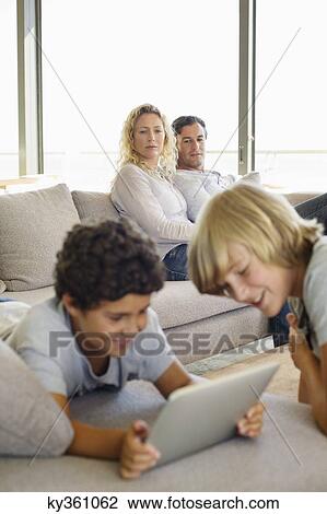 Stock Image - Brothers using a digital tablet with their parents looking at them. Fotosearch