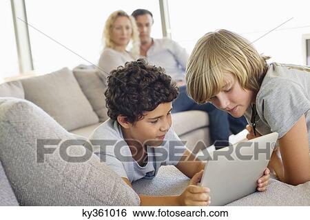 Stock Photograph - Brothers using a digital tablet with their parents looking at them. Fotosearch