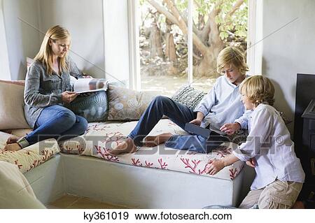 Stock Photo - Children using digital tablet while mother reading magazine at house. Fotosearch
