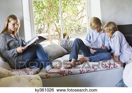 Stock Photograph - Children using digital tablet while mother reading magazine at house. Fotosearch
