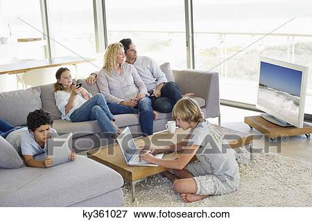 Stock Photo - Couple watching television set while kids busy using electronic gadgets. Fotosearch