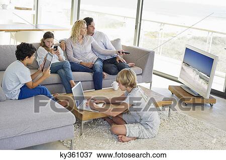 Couple watching television set while their children busy in different activities View Large Photo Image Stock Photo - Couple watching television set while their children busy in different activities. Fotosearch