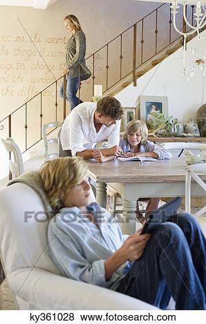 Man talking to little boy with brother using digital tablet in foreground at house View Large Photo Image Stock Photo - Man talking to little boy with brother using digital tablet in foreground at house. Fotosearch
