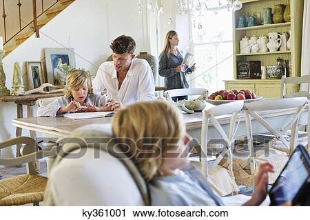 Stock Image - Man teaching little boy while family members busy doing their work at house. Fotosearch