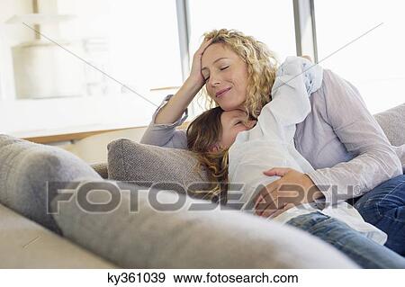 Stock Photo - Mid adult woman and her daughter hugging each other on a couch. Fotosearch