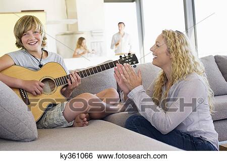 Stock Photograph - Teenage boy playing a guitar with his mother clapping. Fotosearch