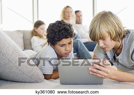Stock Image - Teenage boy using a digital tablet with his brother and his family in the background. Fotosearch