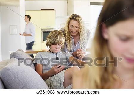 Teenage boy using a digital tablet with his mother looking at him and smiling View Large Photo Image Stock Photo - Teenage boy using a digital tablet with his mother looking at him and smiling. Fotosearch