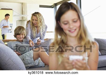 Stock Photo - Teenage boy using a digital tablet with his mother standing behind him and smiling. Fotosearch