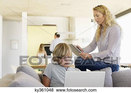 Teenage boy using a laptop and his mother using a digital tablet View Large Photo Image Stock Photo - Teenage boy using a laptop and his mother using a digital tablet. Fotosearch