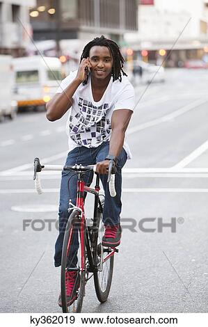 Smiling man talking on a mobile phone while riding a bicycle View Large Photo Image Stock Photo - Smiling man talking on a mobile phone while riding a bicycle. Fotosearch