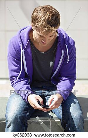 Young man text messaging on a mobile phone View Large Photo Image Stock Image - Young man text messaging on a mobile phone. Fotosearch