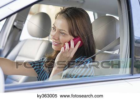 Beautiful young woman talking over mobile phone while driving a car View Large Photo Image Stock Photography - Beautiful young woman talking over mobile phone while driving a car. Fotosearch
