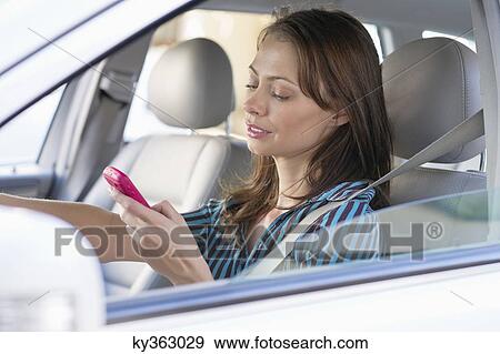 Stock Photo - Beautiful young woman using a mobile phone while driving a car. Fotosearch