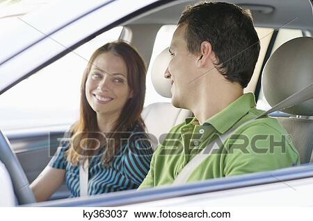 Happy couple looking at each other while driving a car View Large Photo Image Stock Photo - Happy couple looking at each other while driving a car. Fotosearch