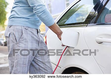 Stock Image - Mid section view of a mid adult man charging the electric car. Fotosearch