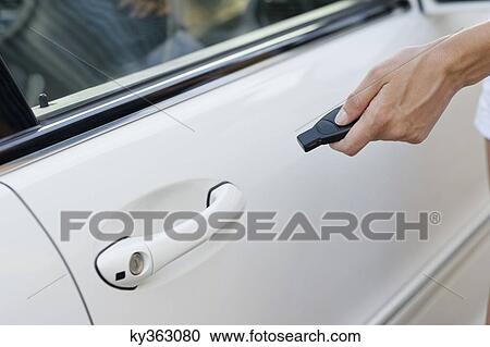 Stock Image - Person's hand unlocking the car with remote control. Fotosearch