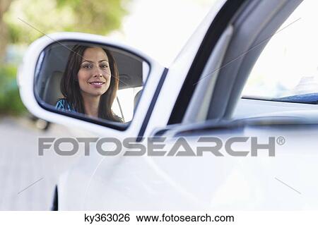 Reflection of a smiling young woman on a car side mirror View Large Photo Image Stock Photograph - Reflection of a smiling young woman on a car side mirror. Fotosearch