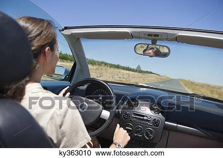 Stock Image - Young woman driving a convertible car. Fotosearch