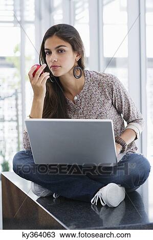 Beautiful woman eating an apple while using a laptop View Large Photo Image Stock Image - Beautiful woman eating an apple while using a laptop. Fotosearch