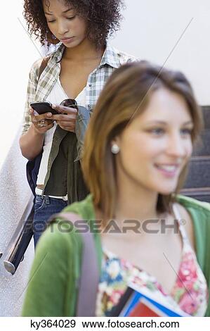 Close-up of a university student with African American woman using mobile phone in the background View Large Photo Image Stock Photo - Close-up of a university student with African American woman using mobile phone in the background. Fotosearch