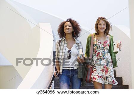 Stock Photograph - Portrait of a beautiful woman walking down stairs with an African American friend. Fotosearch