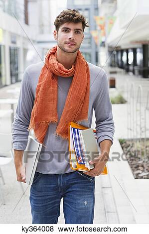 Portrait of a man walking with books and a laptop in hands View Large Photo Image Stock Photo - Portrait of a man walking with books and a laptop in hands. Fotosearch
