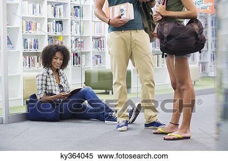 Portrait of university student sitting on the floor with friends standing beside View Large Photo Image Stock Photography - Portrait of university student sitting on the floor with friends standing beside. Fotosearch