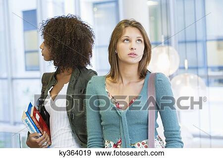 Two women looking away with books in hand at university View Large Photo Image Stock Photo - Two women looking away with books in hand at university. Fotosearch