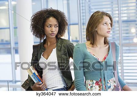 Stock Photo - Two women looking away with books in hand at university. Fotosearch