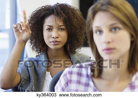 Two women sitting in classroom with focus on African American woman raising hand View Large Photo Image Stock Image - Two women sitting in classroom with focus on African American woman raising hand. Fotosearch