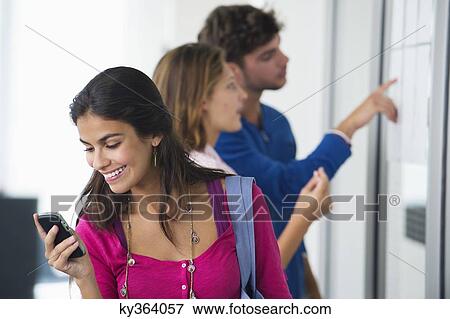University students checking for test results in bulletin board while woman checking text message on mobile phone View Large Photo Image Stock Photo - University students checking for test results in bulletin board while woman checking text message on mobile phone. Fotosearch