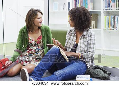 Picture - University students talking while sitting on the floor in a library. Fotosearch