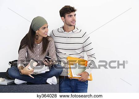 Young friends looking away while holding books and a mobile phone against white background View Large Photo Image Stock Photo - Young friends looking away while holding books and a mobile phone against white background. Fotosearch