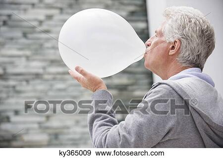 Stock Photo - Close-up of a senior man blowing a balloon. Fotosearch