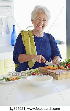 Portrait of a senior woman cutting vegetable in a kitchen View Large Photo Image Stock Image - Portrait of a senior woman cutting vegetable in a kitchen. Fotosearch