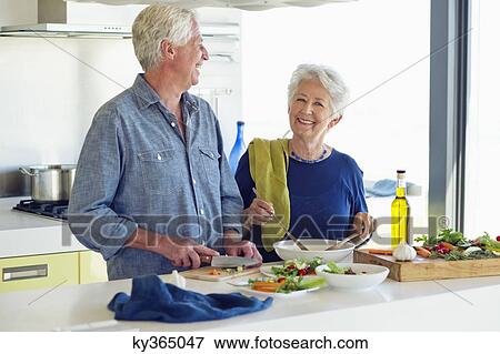 Senior couple preparing food at a domestic kitchen View Large Photo Image Stock Photo - Senior couple preparing food at a domestic kitchen. Fotosearch