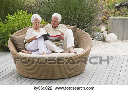 Senior couple sitting in a wicker couch reading a magazine View Large Photo Image Stock Image - Senior couple sitting in a wicker couch reading a magazine. Fotosearch