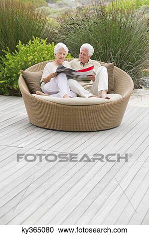 Senior couple sitting in a wicker couch reading a magazine View Large Photo Image Stock Image - Senior couple sitting in a wicker couch reading a magazine. Fotosearch