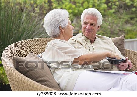 Senior couple sitting in a wicker couch eating food View Large Photo Image Stock Photograph - Senior couple sitting in a wicker couch eating food. Fotosearch