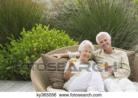 Senior couple sitting in a wicker couch holding wine glasses View Large Photo Image Stock Photograph - Senior couple sitting in a wicker couch holding wine glasses. Fotosearch